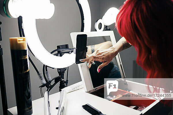 Gefärbte Haare  weibliche Stylistin  die ein Smartphone benutzt  während sie im Studio vloggt