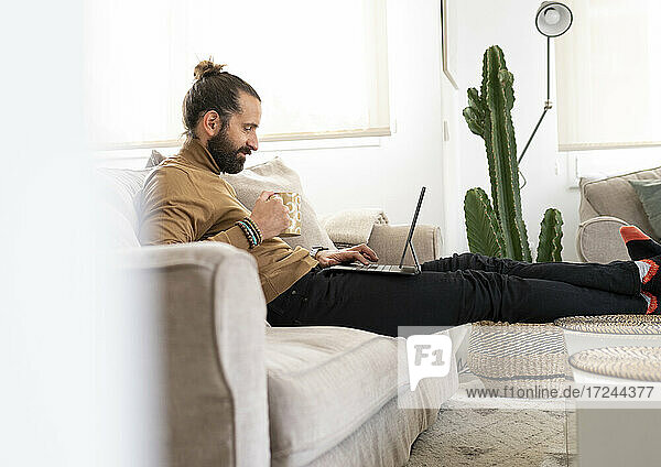 Entspannter Mann mit Tablet-PC auf dem Sofa im heimischen Wohnzimmer