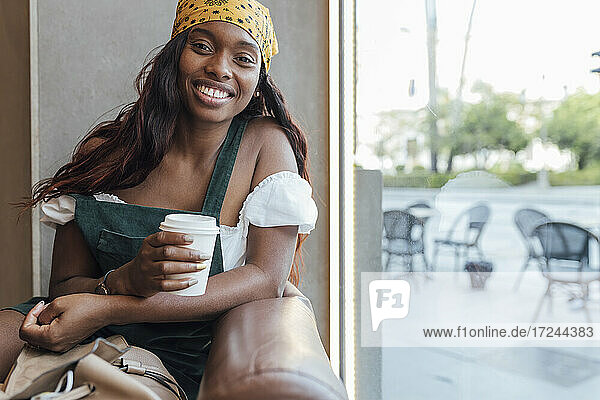 Frau mit Kaffeetasse sitzt am Glasfenster eines Cafés