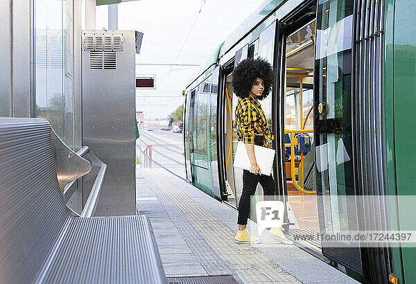 Afro-Frau mit Laptop beim Einsteigen in den Zug am Bahnhof