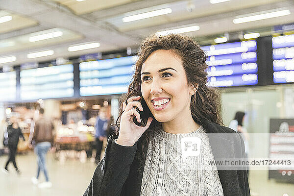 Glückliche Geschäftsfrau  die wegschaut  während sie mit einem Mobiltelefon spricht