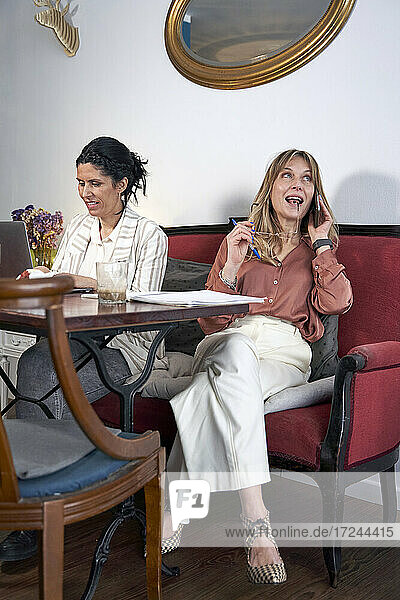 Geschäftsfrau  die einen Laptop benutzt  während sie mit einer Kollegin zusammensitzt  die in einem Café mit einem Mobiltelefon spricht