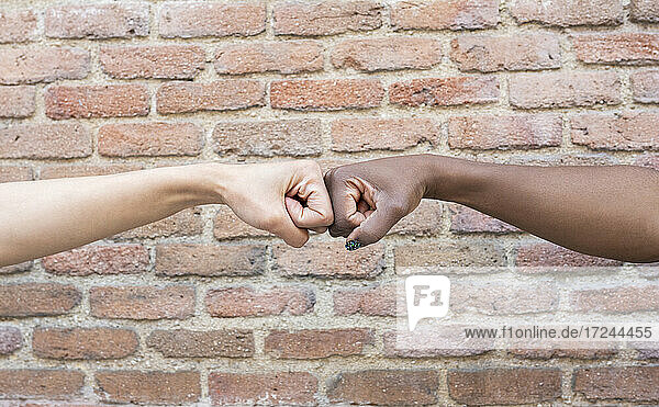 Female friends giving fist bump by brick wall