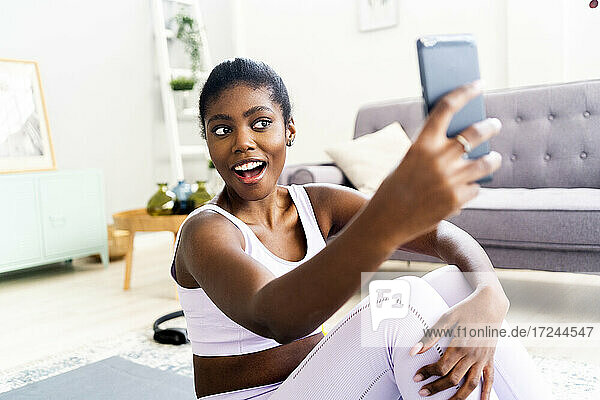 Junge Frau in Sportkleidung  die ein Selfie macht  während sie zu Hause sitzt