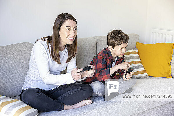 Neugierige Mutter spielt Videospiel mit ihrem Sohn auf dem Sofa zu Hause