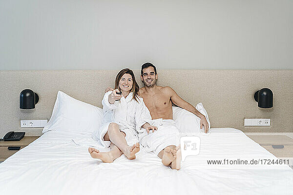 Relaxed couple watching TV while sitting on bed in hotel room