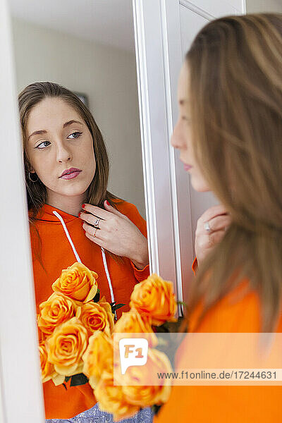 Junge Frau mit orangefarbenen Blumen vor dem Spiegel