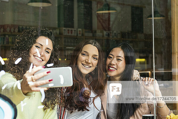 Freunde machen ein Selfie mit dem Handy am Fenster eines Cafés