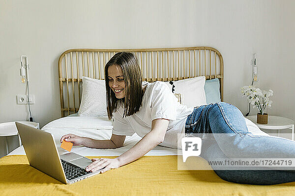 Happy woman doing home shopping through credit card on bed