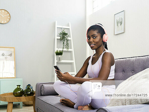 Lächelnde Frau mit Kopfhörern bei der Benutzung eines Mobiltelefons zu Hause