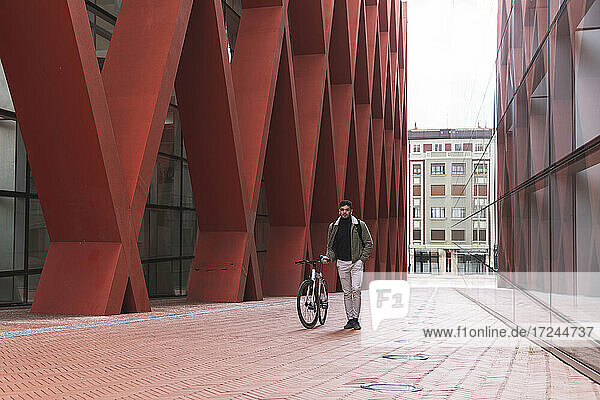 Männlicher Fachmann  der ein Fahrrad vor einem Bürogebäude in der Stadt fährt