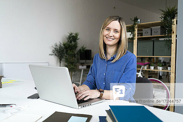Lächelnde Geschäftsfrau beim Tippen auf einem Laptop im Büro