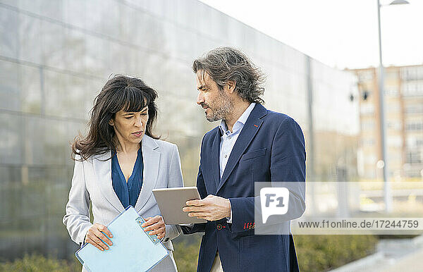 Geschäftsmann  der mit einer Kollegin im Büropark über ein digitales Tablet diskutiert