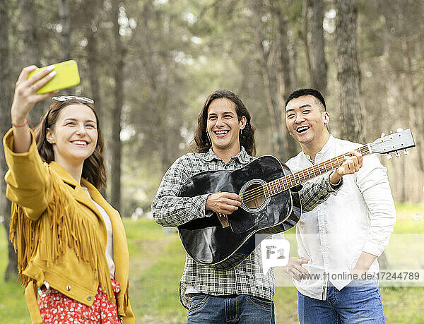 Beautiful woman taking selfie with male friends on picnic at forest