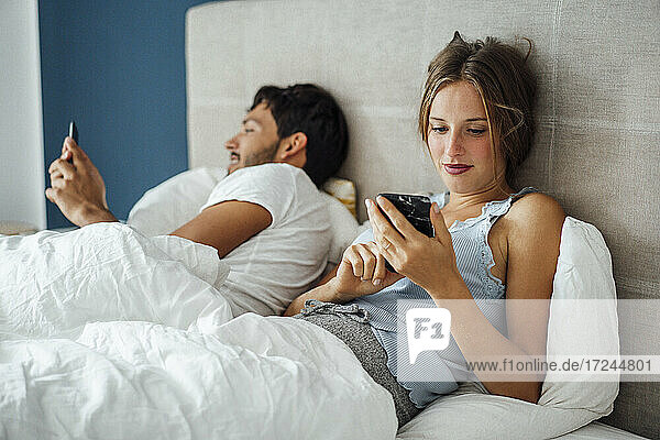 Young couple using smart phone while lying on bed at home
