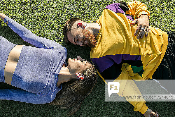 Smiling man lying by woman on grass during sunny day