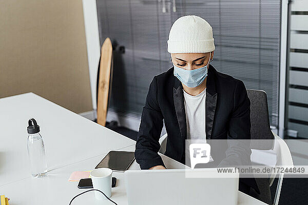Junge Unternehmerin mit Schutzmaske bei der Arbeit am Laptop im Büro