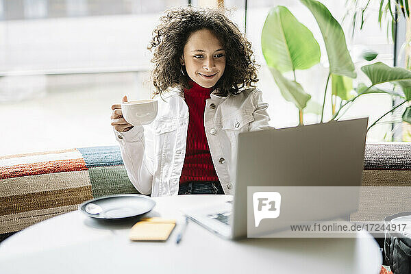 Schöne Frau hält eine Kaffeetasse und benutzt einen Laptop in einem Café