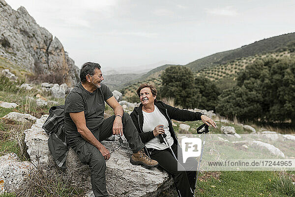 Älteres Paar beim Wandern in den Bergen  das lächelnd auf einem Felsen sitzt