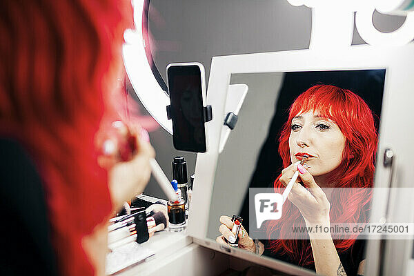 Weibliche Vloggerin trägt Lippenstift auf und betrachtet ihr Spiegelbild im Studio
