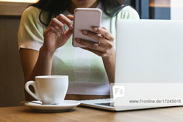 Frau mit Laptop und Kaffeetasse  die ihr Smartphone in einem Café benutzt