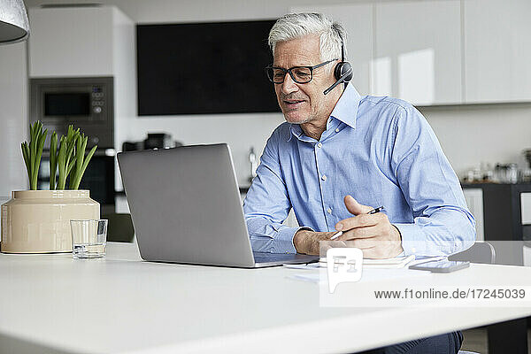 Älterer Berufstätiger mit drahtlosem Headset  der ein Videogespräch über einen Laptop im Büro führt