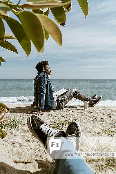Entspannter Mann mit Buch am Strand sitzend an einem sonnigen Tag