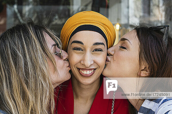 Female friends kissing beautiful woman on cheek outdoors