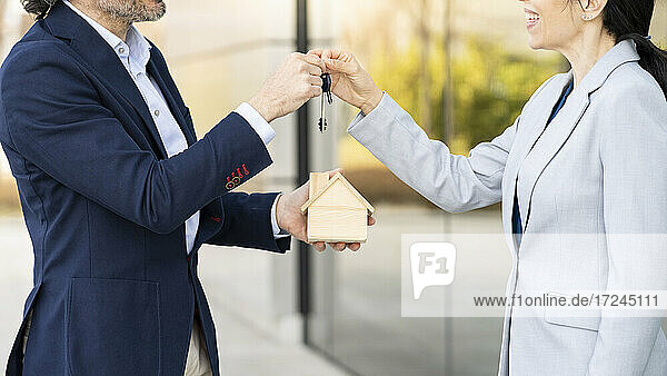 Männlicher Immobilienentwickler mit Architekturmodell  der einer Geschäftsfrau einen Hausschlüssel übergibt