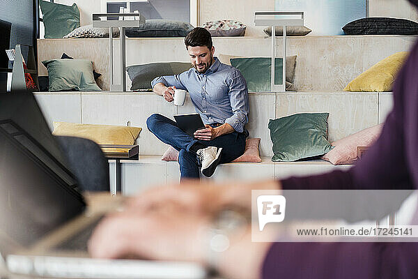 Mid adult businessman with coffee cup working on digital tablet at work place