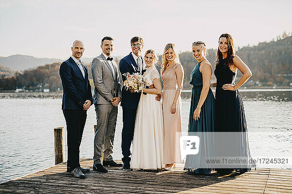 Braut und Bräutigam stehen zusammen mit Freunden auf einem Steg über dem See