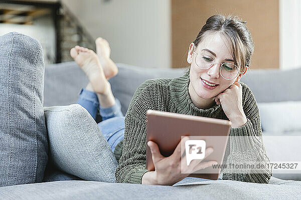Frau mit Brille benutzt digitales Tablet auf dem Sofa zu Hause
