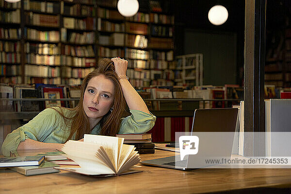 Ernste Frau mit Hand im Haar in der Bibliothek sitzend