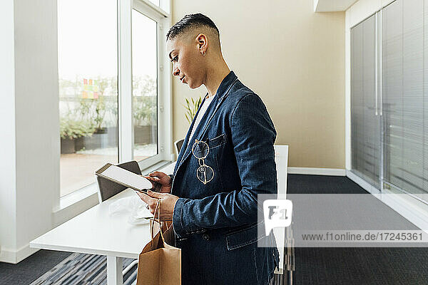 Junger Unternehmer mit Papiertüte und digitalem Tablet im Büro
