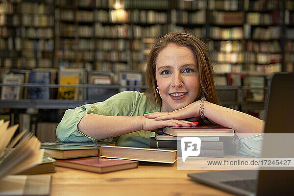 Lächelnde Frau  die sich in einer Bibliothek auf Bücher stützt