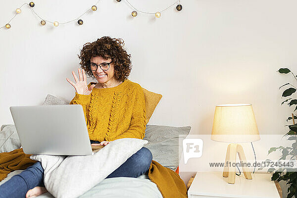 Lächelnde Frau winkt bei Videoanruf über Laptop zu Hause