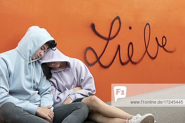 Junges Paar kuschelt vor deutschem Wort für Liebe auf orangefarbener Wand