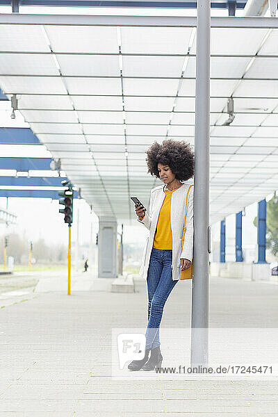 Weibliche Fachkraft  die ihr Smartphone benutzt  während sie sich an eine architektonische Säule am Bahnhof lehnt