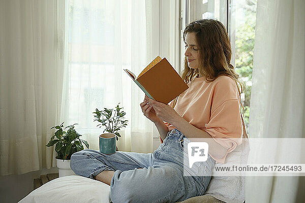 Frau liest ein Buch  während sie zu Hause auf einer Matratze sitzt