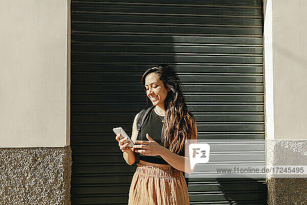 Smiling female tourist using smart phone while standing in front of shutter