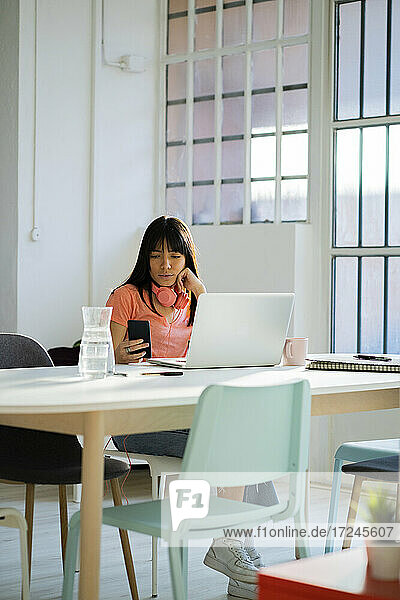 Berufstätige Frau mit Laptop und Smartphone am Tisch sitzend