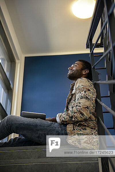 Lächelnder junger Mann mit digitalem Tablet auf einer Treppe sitzend