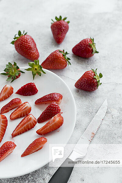 Küchenmesser und Teller mit frischen Erdbeeren auf weißem Marmor liegend