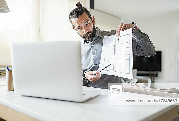 Male design professional showing construction plan on video call over laptop at home