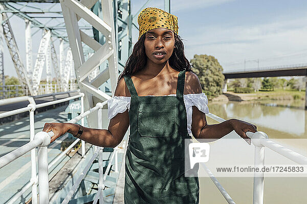 Frau steht auf einer Brücke und hält das Geländer an einem sonnigen Tag