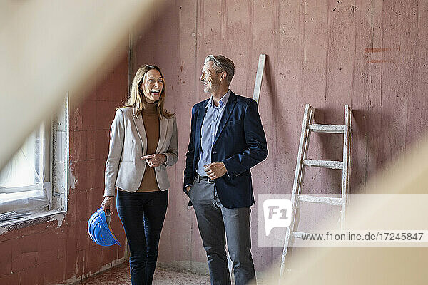 Lächelnde weibliche Kollegin im Gespräch mit einem männlichen Architekten auf der Baustelle