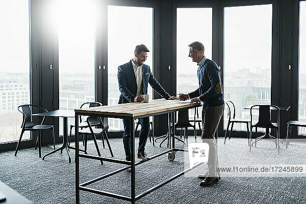 Lächelnde männliche Geschäftsleute im Gespräch am Tisch im Büro-Café