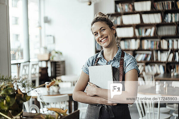 Cheerful mid adult waitress holding digital tablet at cafe