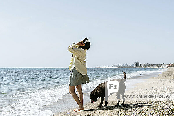 Frau hört Musik über Kopfhörer bei einem Hund am Strand