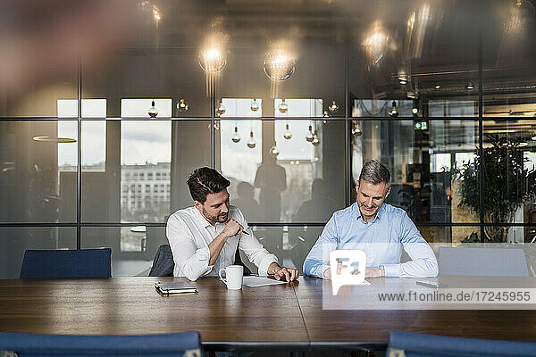 Männlicher Unternehmer schreibt auf Papier  während er mit einem Kollegen im Sitzungssaal arbeitet